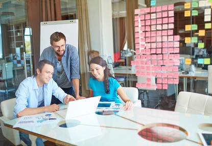 Group of business partners in casual listening to young man pointing at laptop screen in office